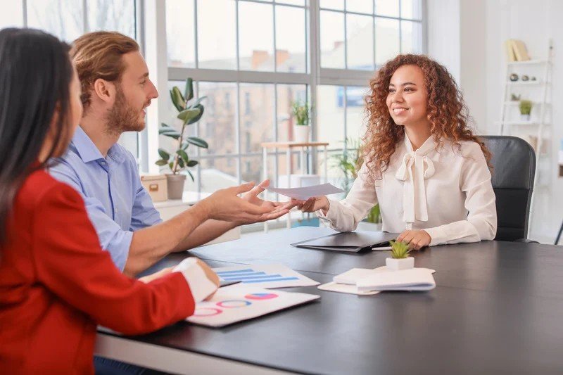 A program coordinator handing paperwork across a table in a bright meeting room